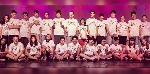 Em um palco de teatro, os atores com espectro autista posam para a foto, disposto lado a lado e sentados no chão