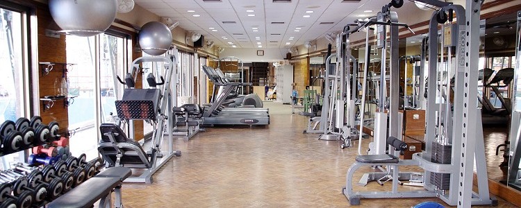 Foto de uma academia de ginástica vazia. Há vários aparelhos de musculação, com halteres e pesos de diferentes formatos e tamanhos.