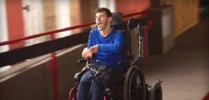 Homem jovem com deficiência em cadeira de rodas automatizada em corredor iluminado