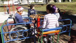 Quatro crianças com idade média de 8 anos brincam em um gira-gira inclusivo; uma delas é cadeirante