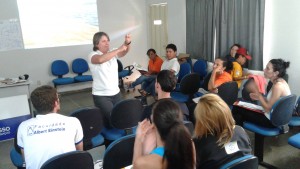 Professora gesticula perante turma de alunos.