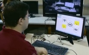 Um homem jovem sentado em frente a um computador, acessando-o sem o uso de teclado ou mouse