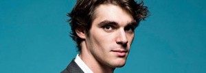 RJ Mitte, ator de Breaking Bad, está em close, olhando para a câmera. Ele usa uma roupa social e está sobre um fundo verde.