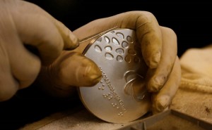 Foto de mãos com luvas cirúrgicas manuseando a medalha paralímpica durante a produção