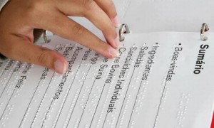 Foto de uma jovem mão feminina tateia um cardápio com informações em braile