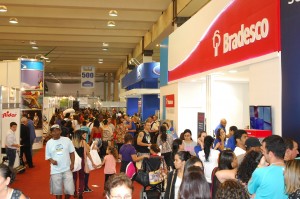 Foto de um pavilhão com multidão visitando stands de diversas empresas.