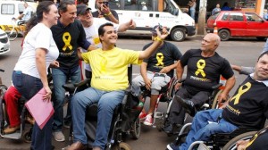 Foto de um estacionamento. Em destaque, cadeirantes de diversas idades ocupam vagas para carros. Eles sorriem e gesticulam