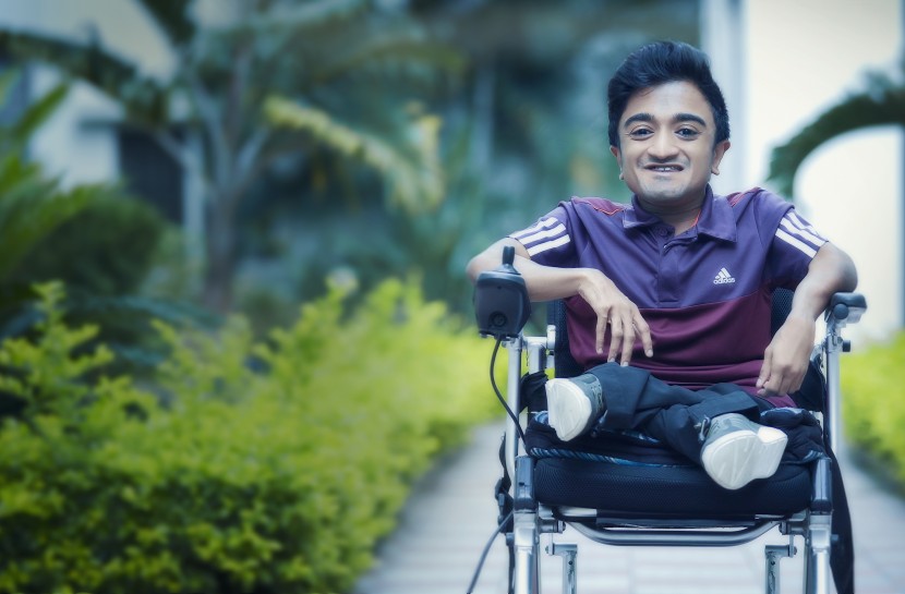 Foto de Jeevan em sua cadeira de rodas em uma calçada.