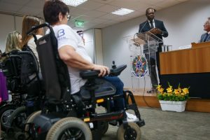 Foto do interior de uma sala de conferências. Silvio Almeida, ministro dos Direitos Humanos e Cidadania, fala em um microfone para um grupo de pessoas cadeirantes.