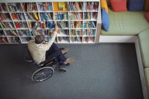 Foto de uma pessoa cadeirante pegando um livro de uma estante.
