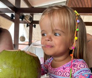 Foto de uma criança com nanismo que toma água de coco com um canudo.