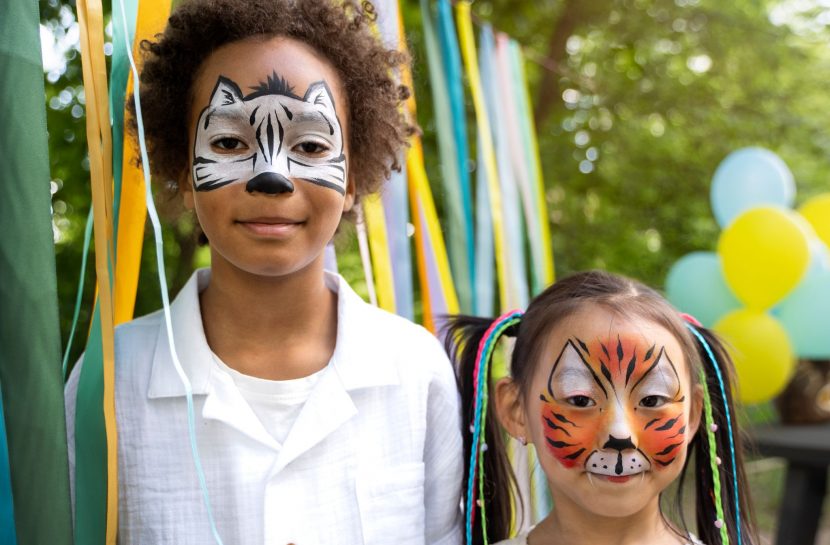 Um menino e uma menina têm os rostos pintados com figura de animais. Os dois sorriem para a câmera.