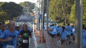 Pessoas correndo com camisa azul do Instituto Olga Kos numa avenida larga, totalmente cheia de pessoas