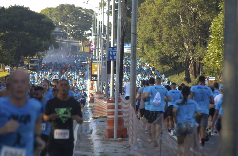 Pessoas correndo com camisa azul do Instituto Olga Kos numa avenida larga, totalmente cheia de pessoas