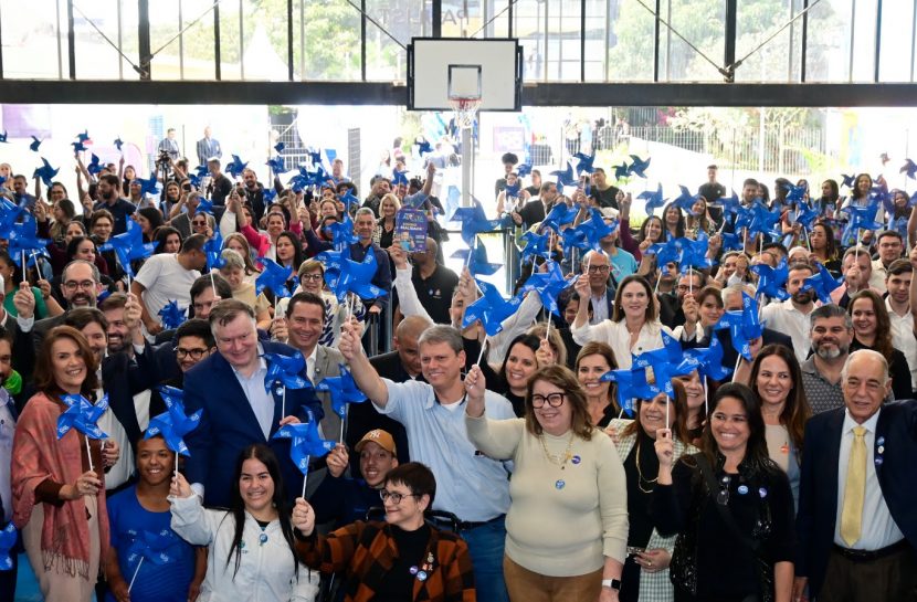Grupo grande de pessoas diversas na inauguração do Centro. Todas seguram cata-ventos azuis para o alto.
