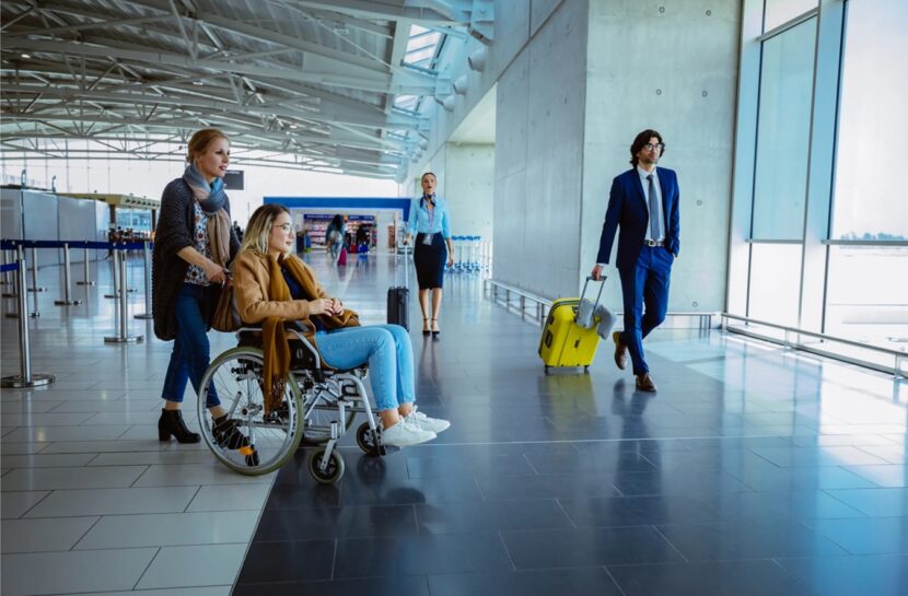 Mulher cadeirante é empurrada por outra mulher em ambiente de aeroporto